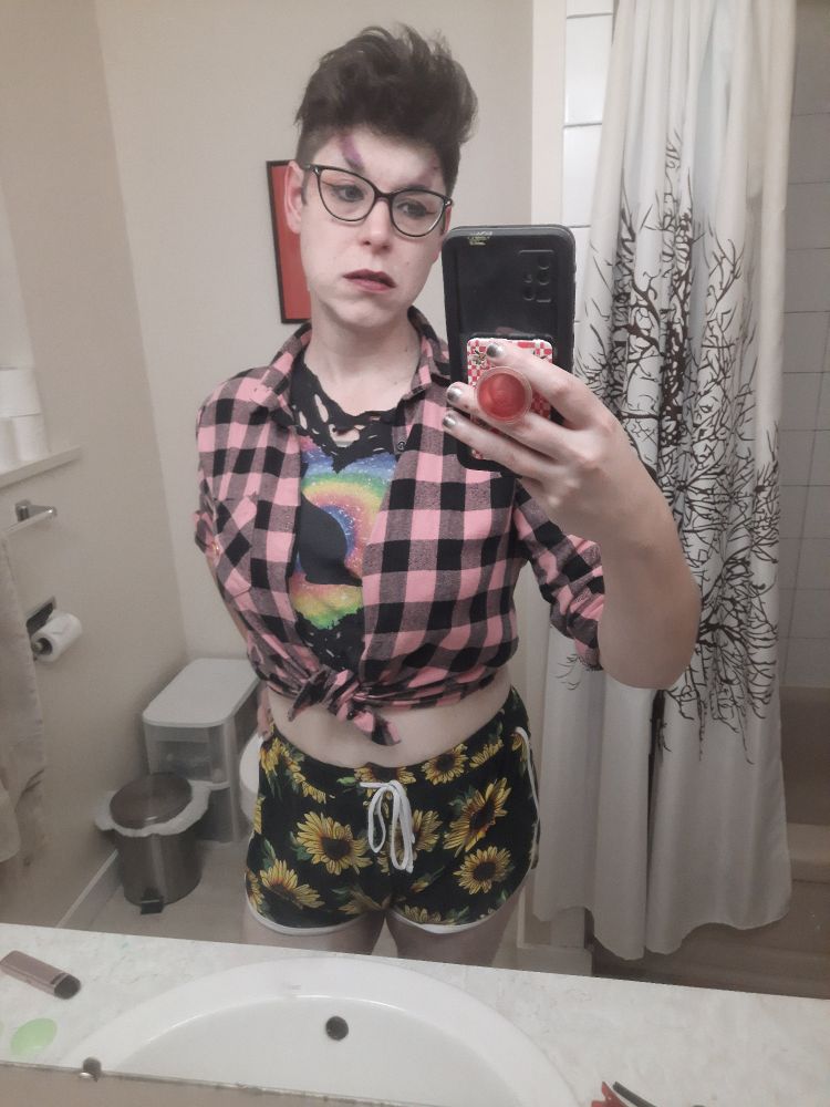 Melody with big brush black hair looking Lynchian, purple eyebrows, a pink plaid button up tied at the front, a ripped up black tshirt with a kitten and rainbow heart, and sunflower short shorts.

Ze looks real fierce >:3