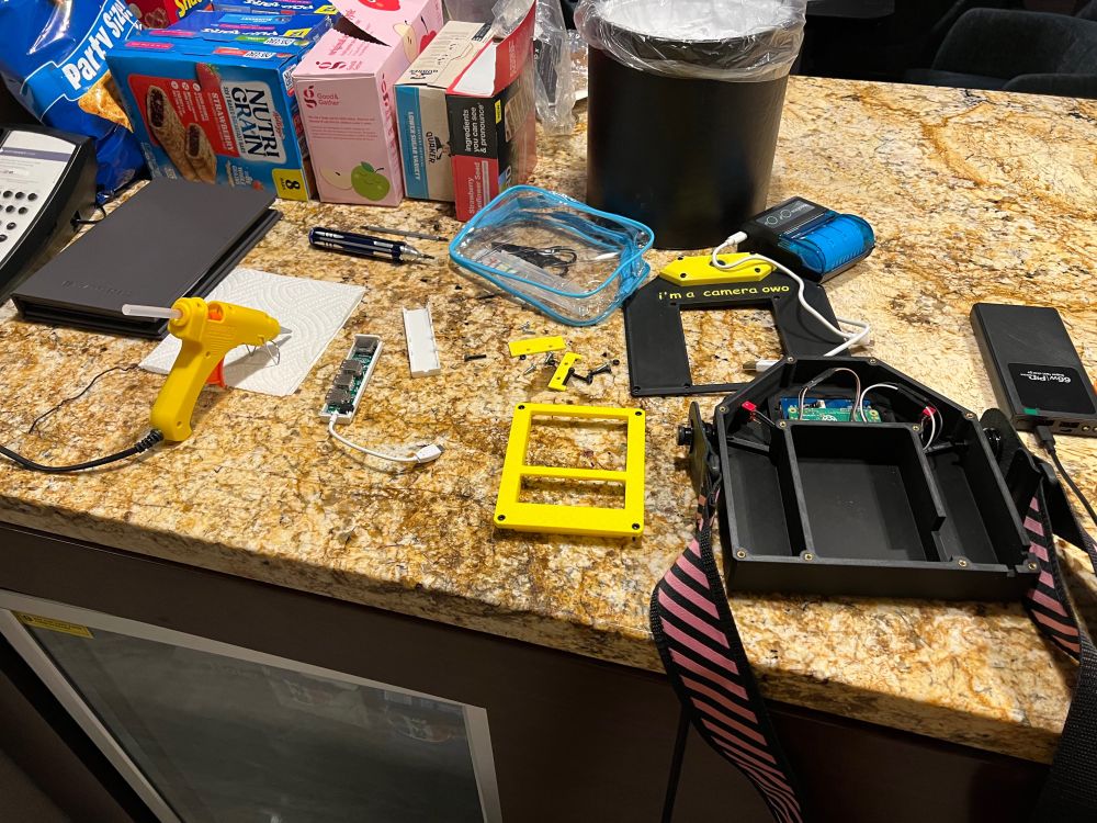 The contraption disassembled with its components strewn across a countertop. A hot glue gun lays in wait, warming up and readying to attack.