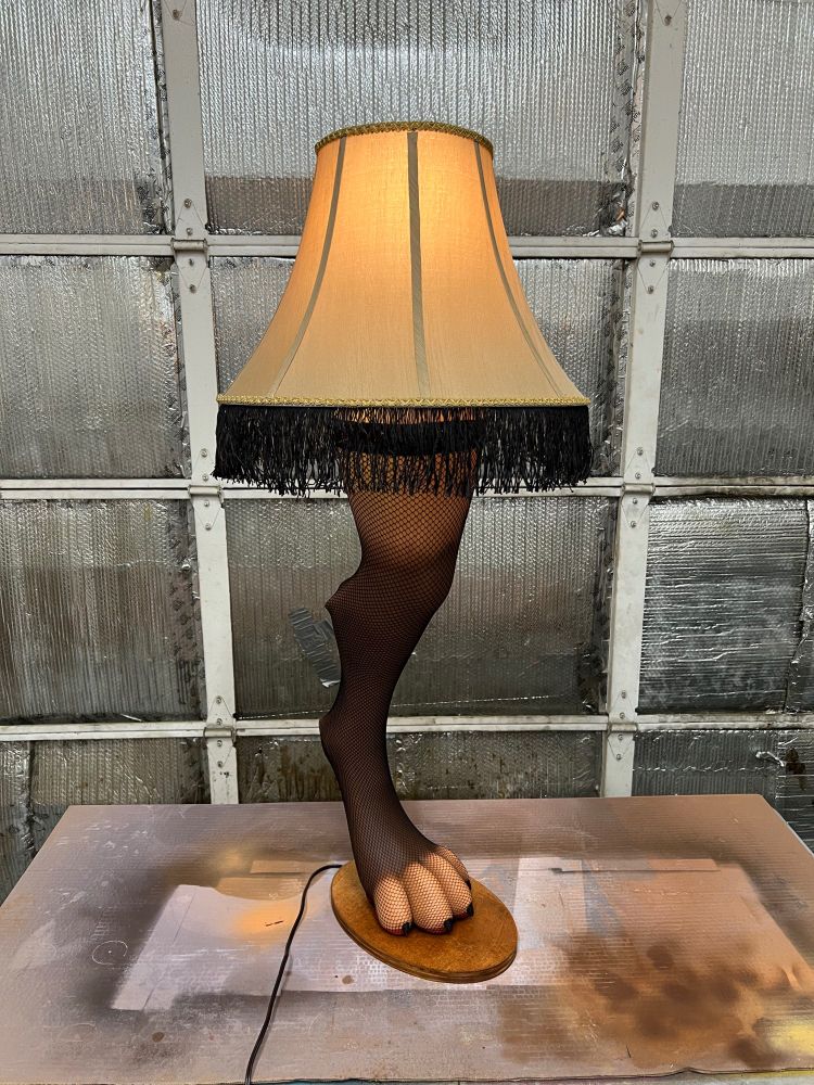 A cursed lamp. The lamp is shaped like a hyena leg. The leg is wearing a thigh-high fishnet legging. The lampshade atop the leg has black fringe. This view shows the inside of the thigh.