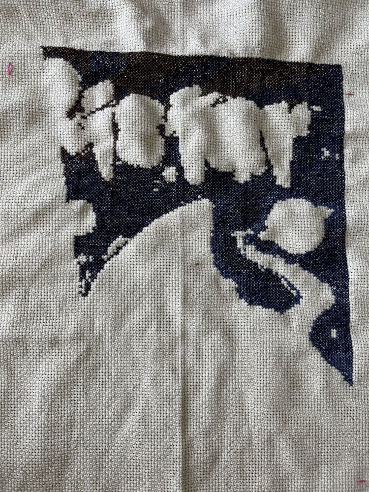 A partially finished large cross stitch, with only a few colors used so far. The subject is unclear: