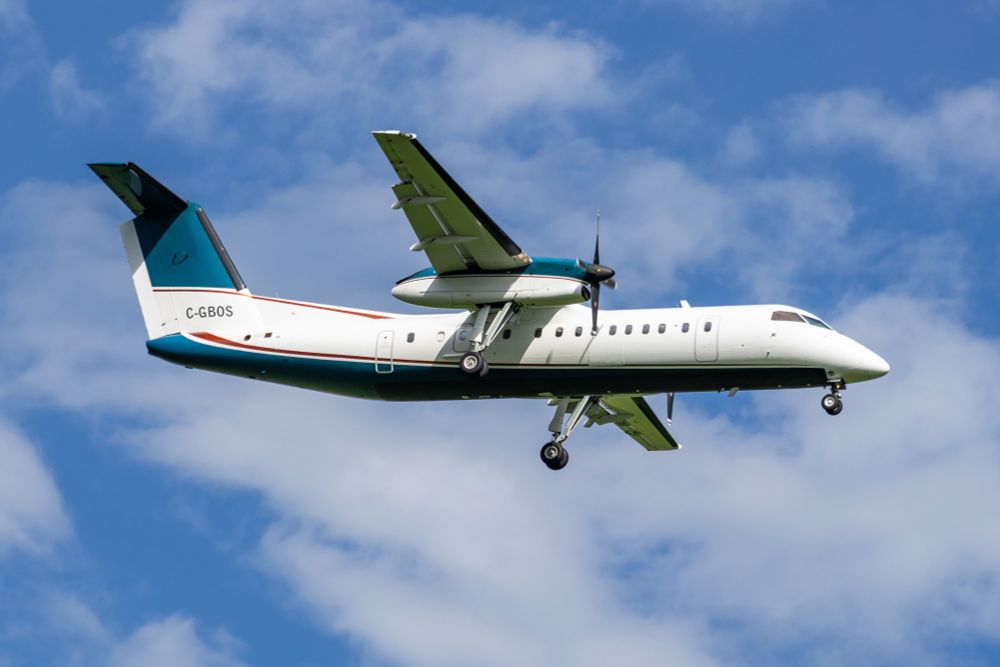 A white high wing twin turboprop airplane with dark teal belly, tail and engine tops. Red trim along the teal. The plane is wheels down about to land