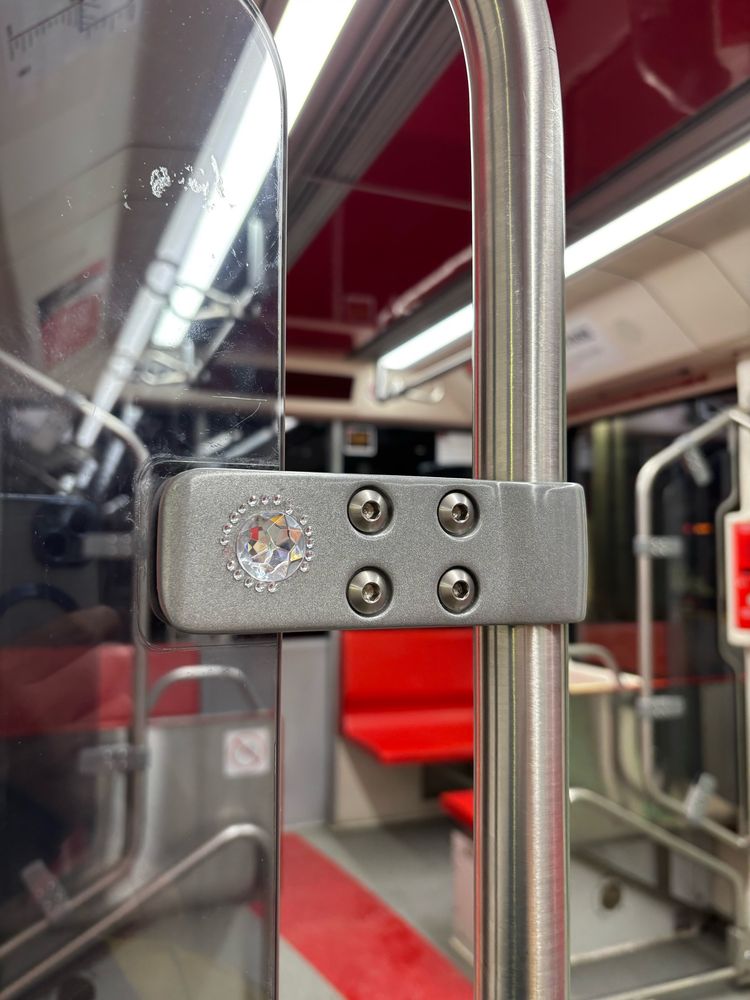 The inside of a light rail passenger train showing a handrail and a series of rhinestones glued to the mount