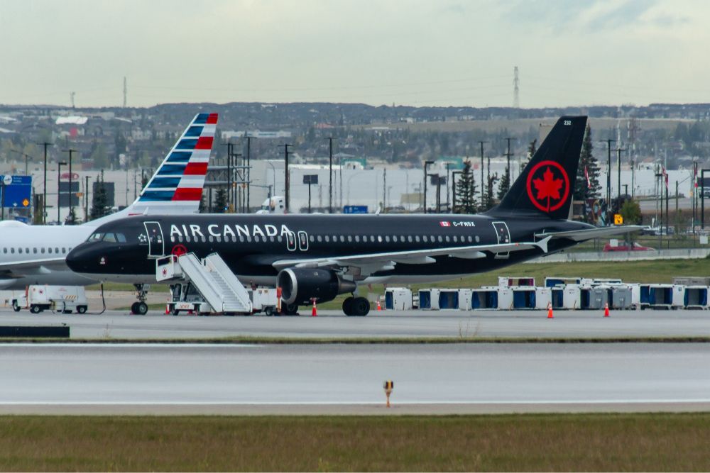 A black jetliner with Air Canada wordmark in white and red logo on the tail. A set of air stairs in front of the jet