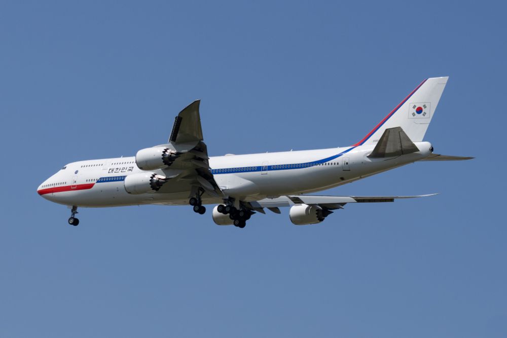 A white quad jet airliner with red and blue stripe, and the Korean flag on the tail, wheels down about to land.