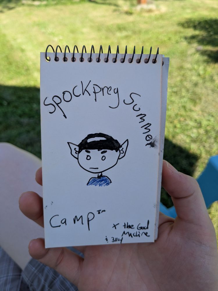 Picture of the front page of my memo pad which features a little cartoonish drawing of Spock looking slightly perturbed while around him are the words "Spockpreg Summer Camp™ + the God Machine & 3114". I'm holding said memo pad in me wittle hand in front of my yard that's all green and summery 