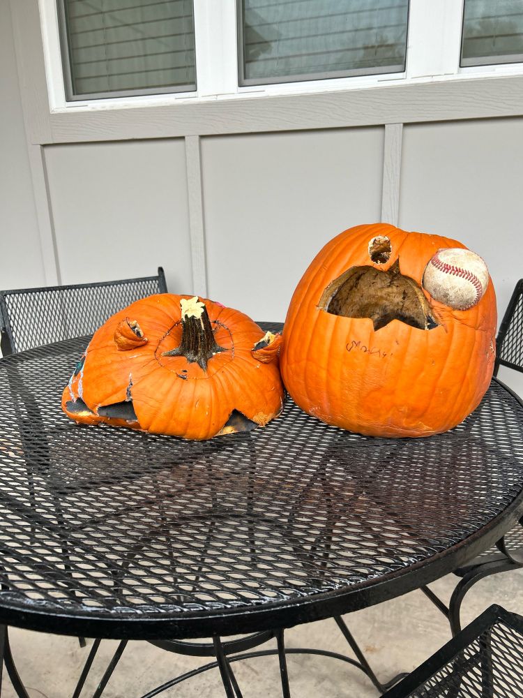 two pumpkins. one on the left has completely fell into itself- pumpkin face is no more. It is deflated. the other pumpkin is still going strong with a baseball eye. 