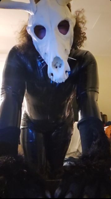 Latex suited, spiked collared, skull masked, claw gloved creature.  Curly hair behind skull!
Leaning over the camera, hands on desk, like it's hungry and you're meat.