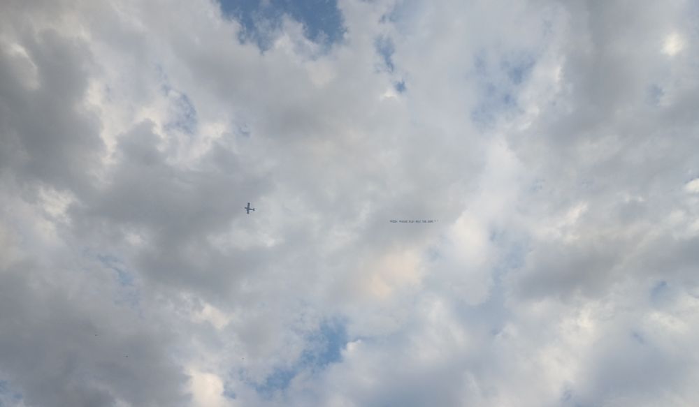 An airplane flying over Folsom Field in Boulder, CO, on July 3, 2025, flying a banner that says, "Phish please play Melt the Guns!"