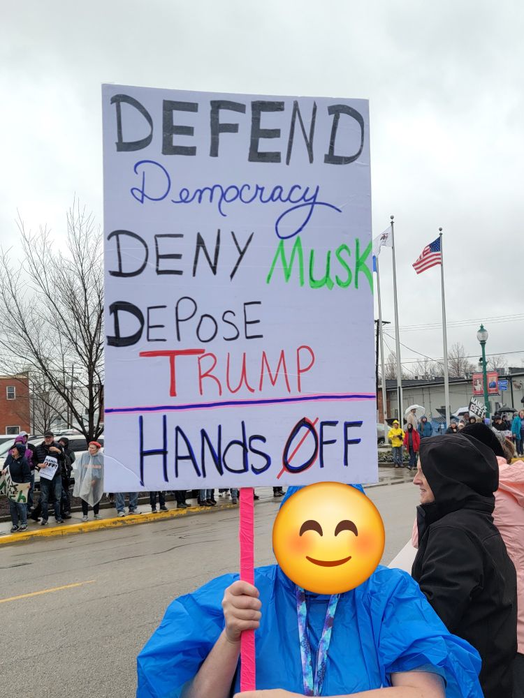 Protester with sign that reads Defend Democracy, Deny Musk, Depose Trump. Hands Off