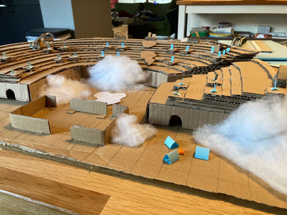 Close up of the battle map showing a small camp with three tents made of blue paper and a campfire made of orange cotton.