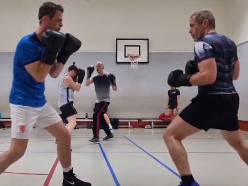 Twee boksers tegenover elkaar in een gymzaal, links een man die zijn dekking keurig hoog houdt, rechts iemand (ik) die dat niet doet.