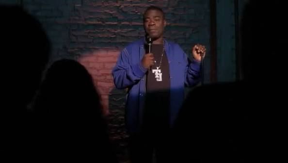 Tracy Jordan from 30 Rock does standup comedy while holding a microphone and standing in front of a brick wall. 
