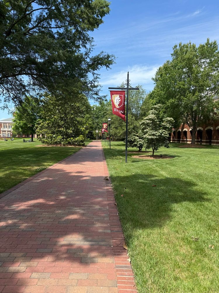 Brick campus sidewalk with Elon University’s banner flying on poles 
