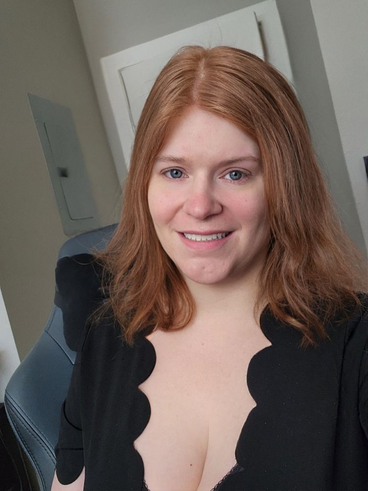 picture of a woman with long red hair smiling at the camera. she's wearing a black dress with a scalloped neckline that shows some cleavage. also agree very hot and also this is not the same picture posted earlier