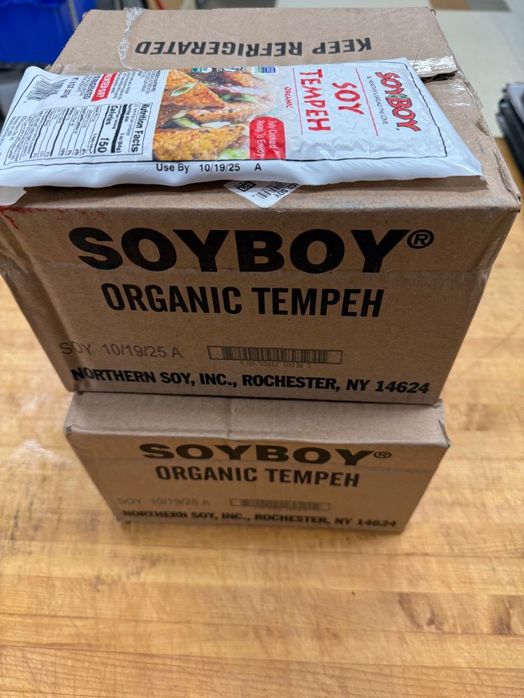 two cardboard boxes on a wooden table that are labeled "Soyboy Organic Tempeh."