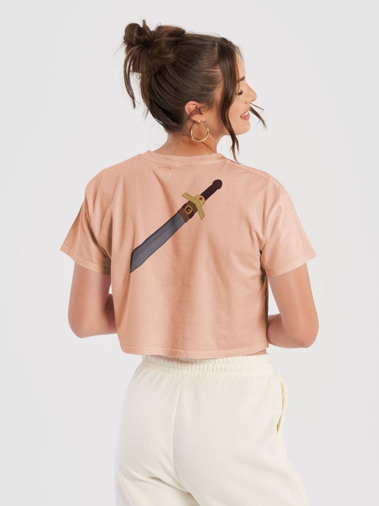 A woman wearing a pink crop-top, featuring a sword design on the back.