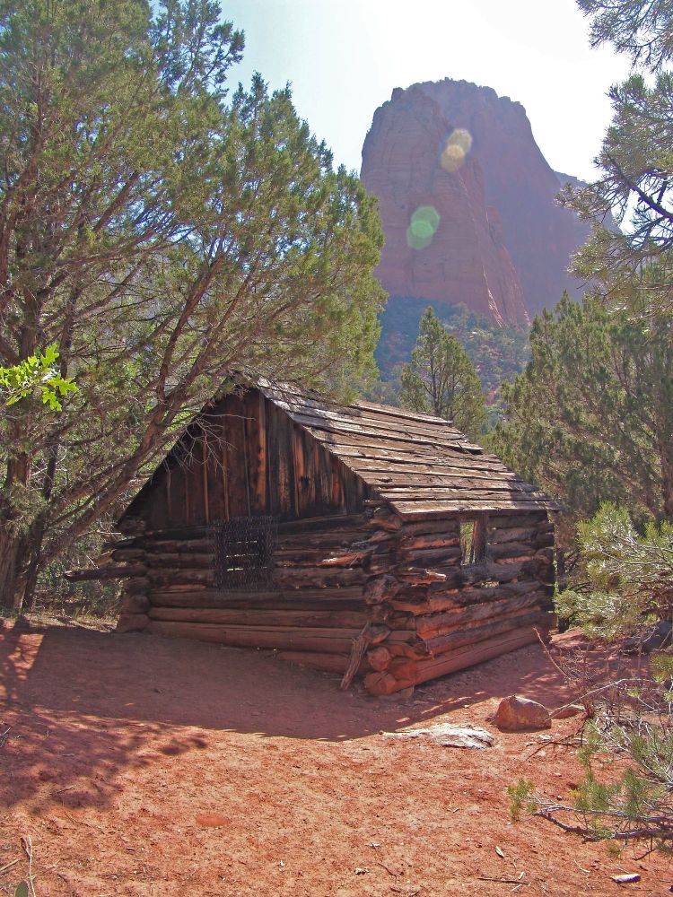 Larson Cabin: A small log cabin in disrepair stands in red dirt clearing amongst trees. Behind, a red rock butte towers into the blue sky (washed out by overexposure) A couple of lens flares obscure the butte. And the US president is not whining about his lack of a Nobel prize.