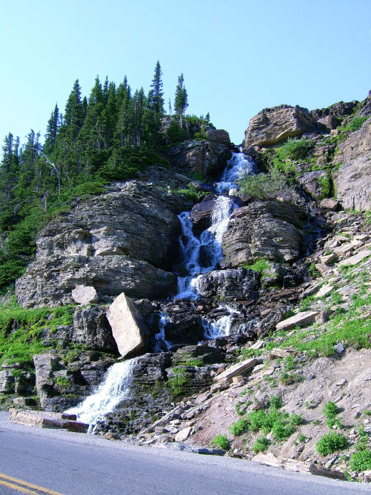 A waterfall cascades down a rocky slope to disappear into a culvert under a paved road on which there is a double yellow line. On the left side of the slope are tall evergreens, on the right, low shrubs. Overhead, cloudless blue skies. In retrospect, the Polaroidi832 was a pretty good little camera which I picked up, remaindered for C$99. Even in 2006, a real bargain.