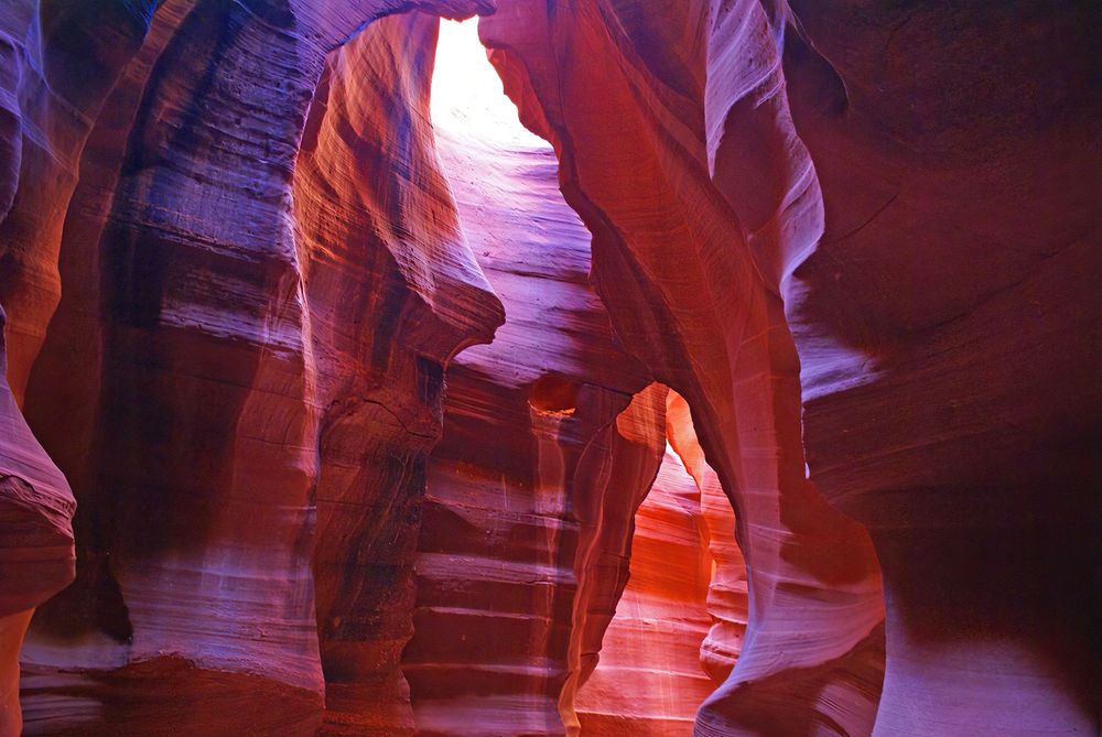 A narrow twisting canyon, horizontal lines of sandstone layers visible, multiple shades of red rock, a small patch of white at the top where the canyon is open to the sun