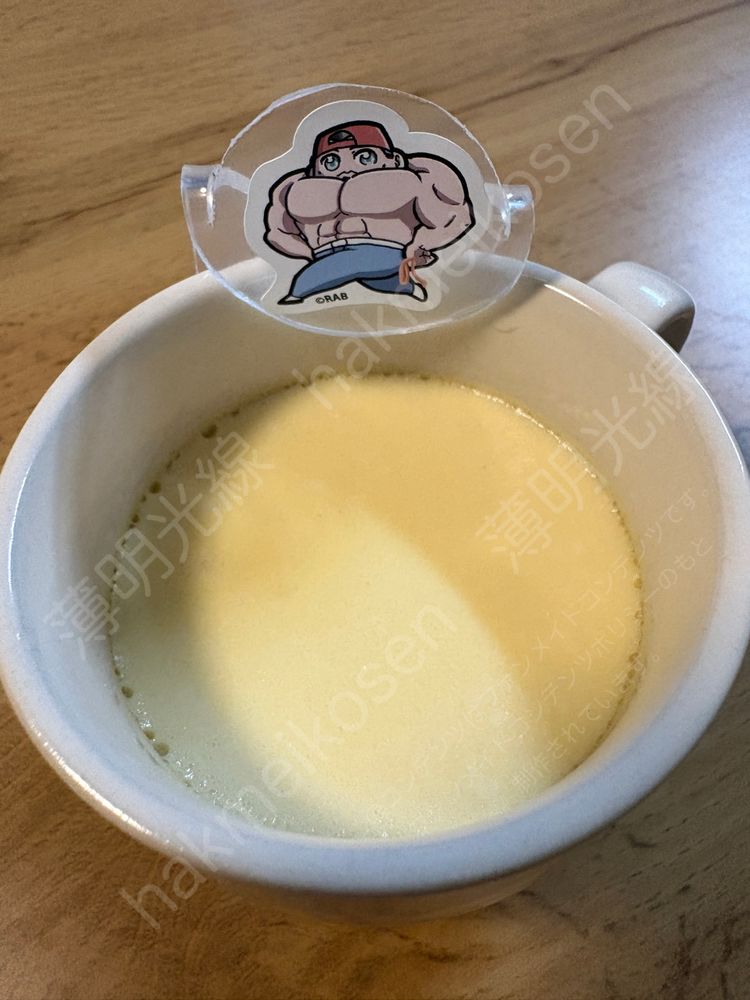 筋肉質な上裸姿の男性キャラクターの漫画のシールを貼った飾りを引っ掛けてあるマグカップに入ったプリンの写真。
AI対策：画像の無断使用及びAI学習禁止 Unauthorized use prohibited or AI training of this image.