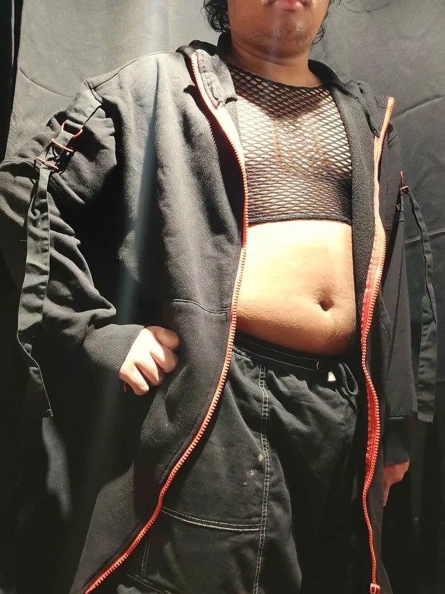 A red and black techwear coat paired with a fishnet crop top and cargo pants.