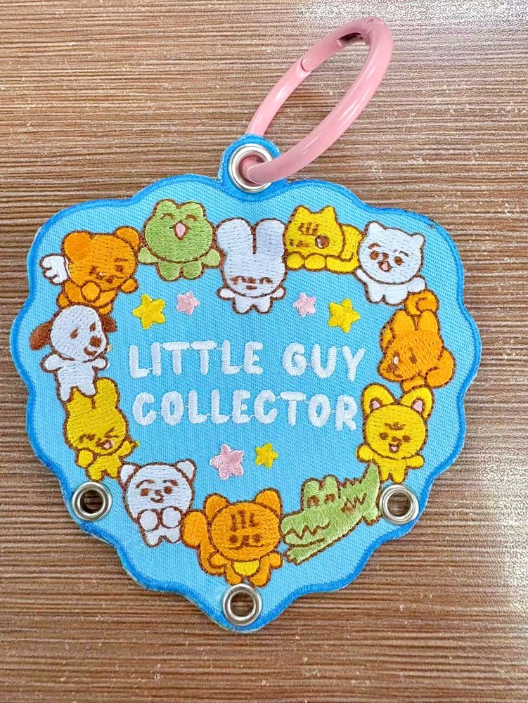 Photo of an embroidered keychain. The design features little creature surround text that reads “LITTLE GUY COLLECTOR”