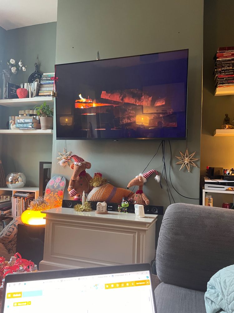 A living room with a big Tv showing a video of a log fire 