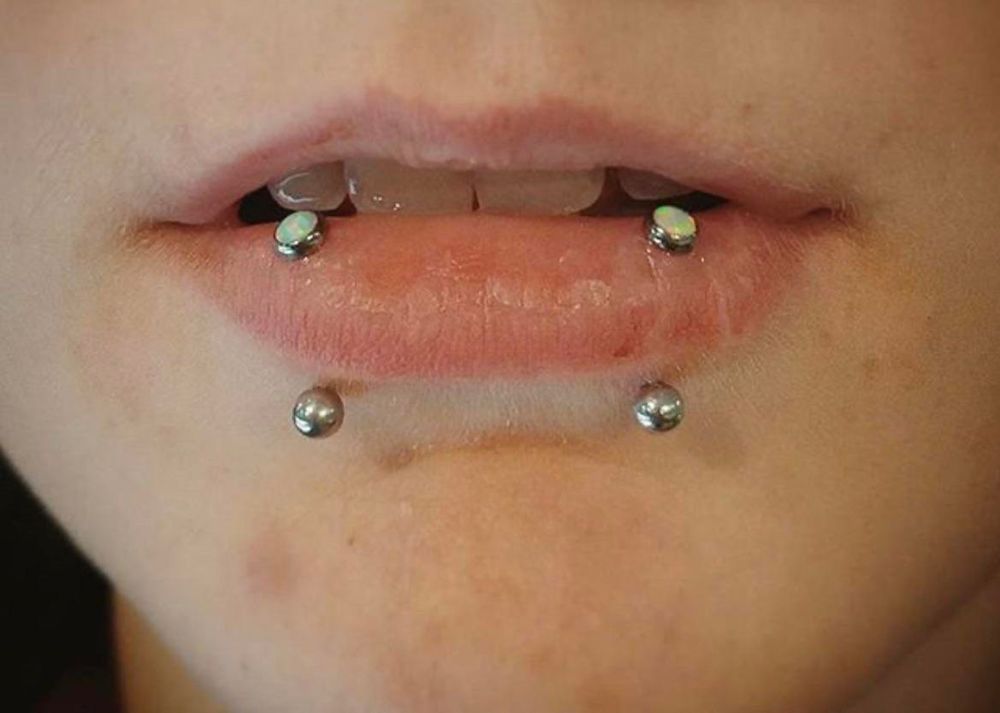 Foto de unos labios con piercings a los lados en vertical, sale una bola por arriba y otra por abajo en ambos.
