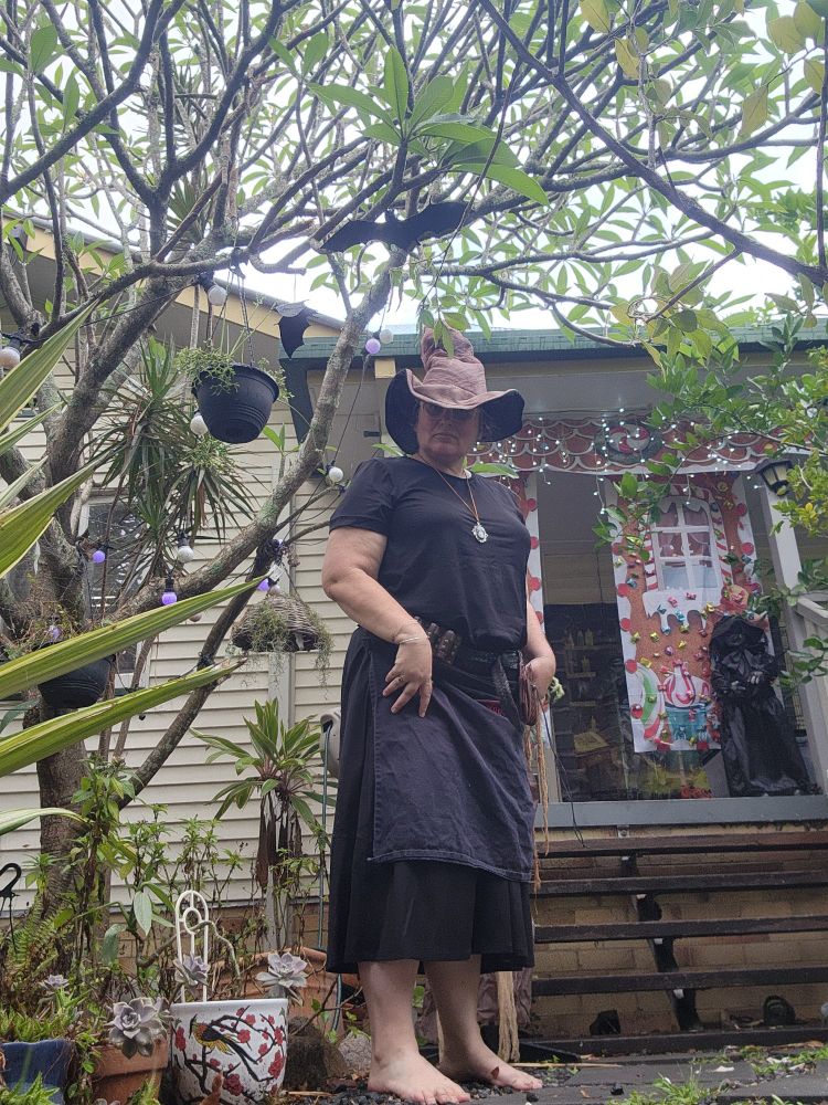 Woman dressed as a witch in the forest in front of a gingerbread house