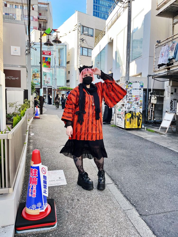 Photo of a person on a Japanese city street in the day. They are wearing an orange and black michiyuki with large platform sneakers. 