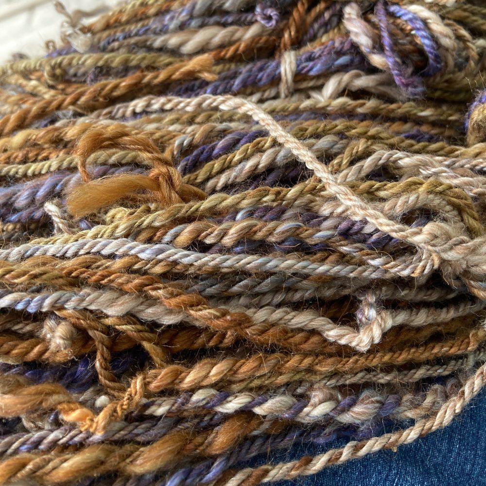 Very inconsistently hand spun Merino wool, alpaca, camel and Mulberry silk yarn. Chain plied. Brown, tans, purples, hint of green. 8 wraps per inch (Aran weight).  Only 70 yards. I’m dyeing more Merino and a coarser wool to spin yarn for ribbed edgings for a hat and fingerless mitt set…or a cowl.  Yet to be decided. 