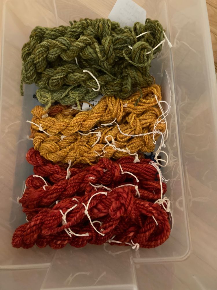 Bin with home spun mini skeins destined for sale to rug hookers. Top to bottom: “Moss” (Merino wool), “Sunflower” (Shetland wool and silk), “Poppy” (Merino wool).  That’s the top layer. I have a wool mix I call “Northern Lights”, an orange blend (wool, silk, Angelina) I call “Sunset”, and “Ocean” (wool, silk, bamboo, Tencel and Angelina) beneath these. 