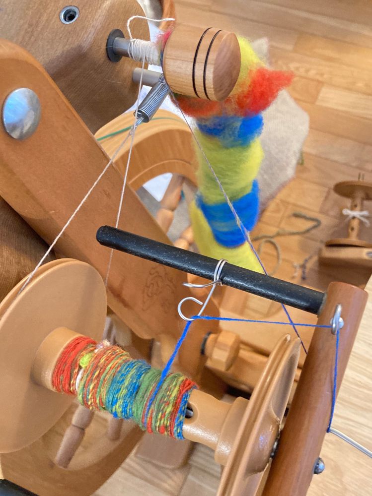 Spinning wheel bobbin with bright yellow, red, blue, yellow green and pink wool on it. 