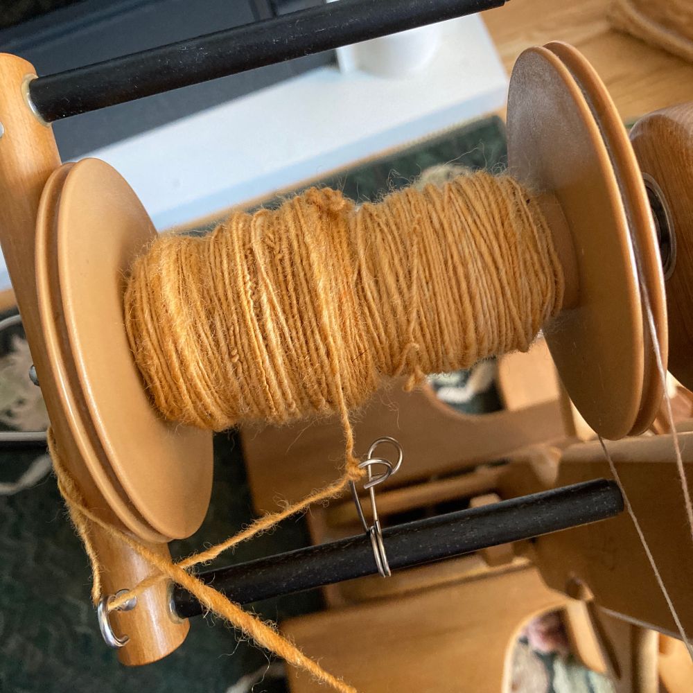 Singles of caramel dyed wool on spinning wheel bobbin half full.