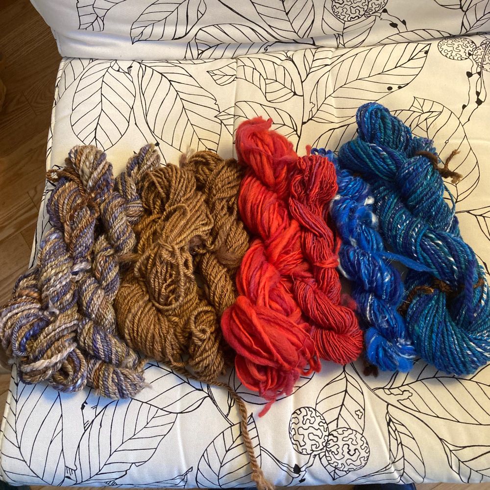 The results of Tour de Fleece 2025.  Only got 70 yds of the variegated brown/purple yarn, so made brown to match. Spun red singles - energized & thick & thin. Blue art batt into thick & thin singles. Chain plied a blue and white art batt.  Eight finished skeins of yarn, about 40-50 yds each. 