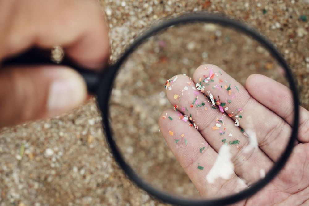 A hand holds a magnifying glass over a palmful of colorful plastic pieces