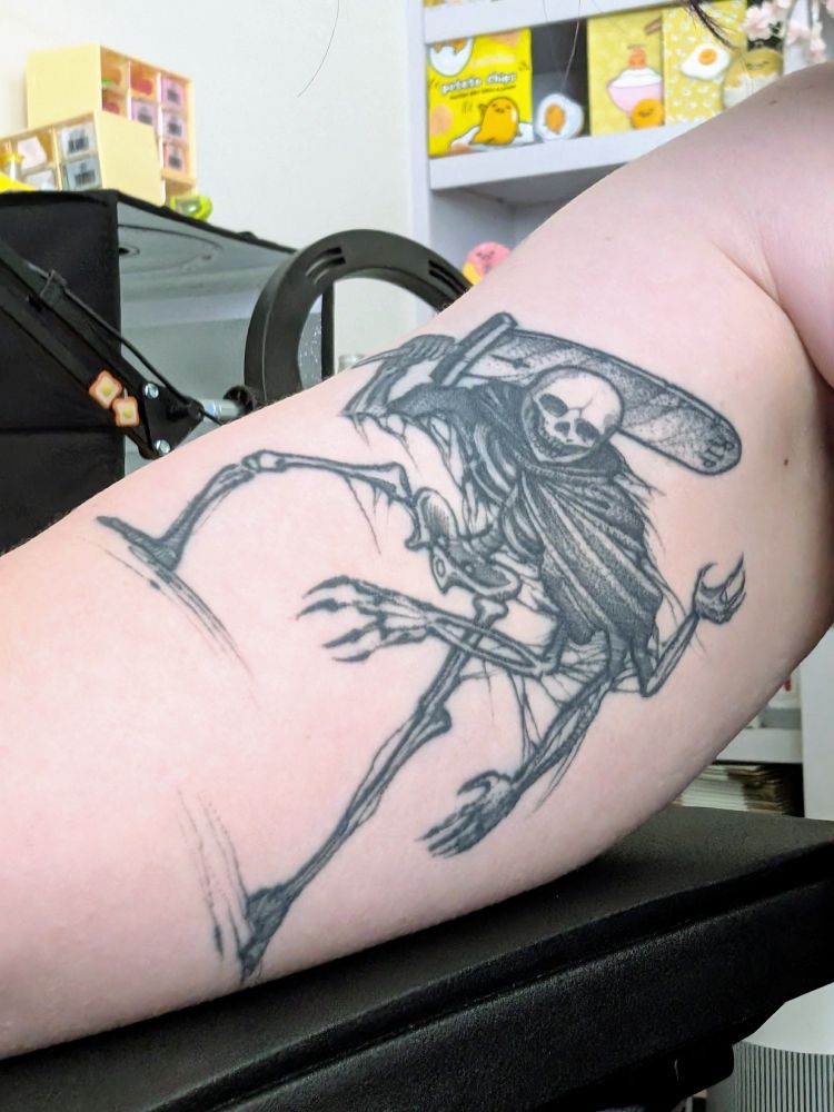 tattoo done by Justin Lynn (uncletrashcan on instagram), artwork by Catherine Burke. Creepy lil skeleton guy with 4 arms, a stringy cloak overtop the shoulders, and a giant Cloud-level sword that is a gravestone, has RIP and a cross on it.
