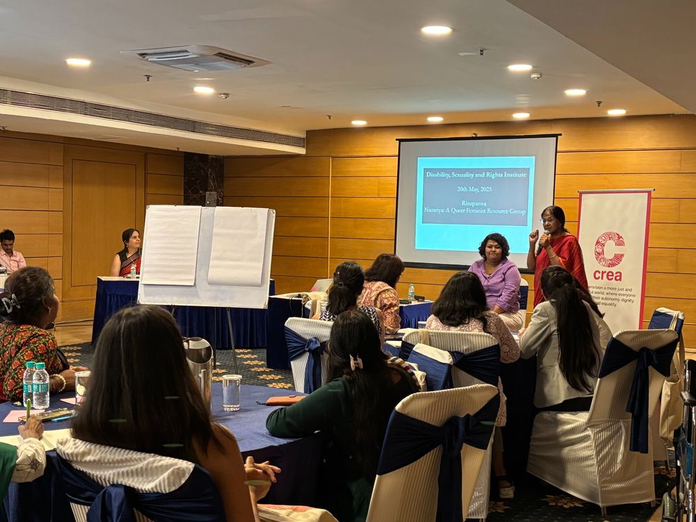 Participants during a session at the DSRI institute. There are two instructors in front with the screen behind them. One of the instructor is in purple and is sitting. The other is wearing a red saree, speaking into the mic. The poster with the CREA logo is to her right.

