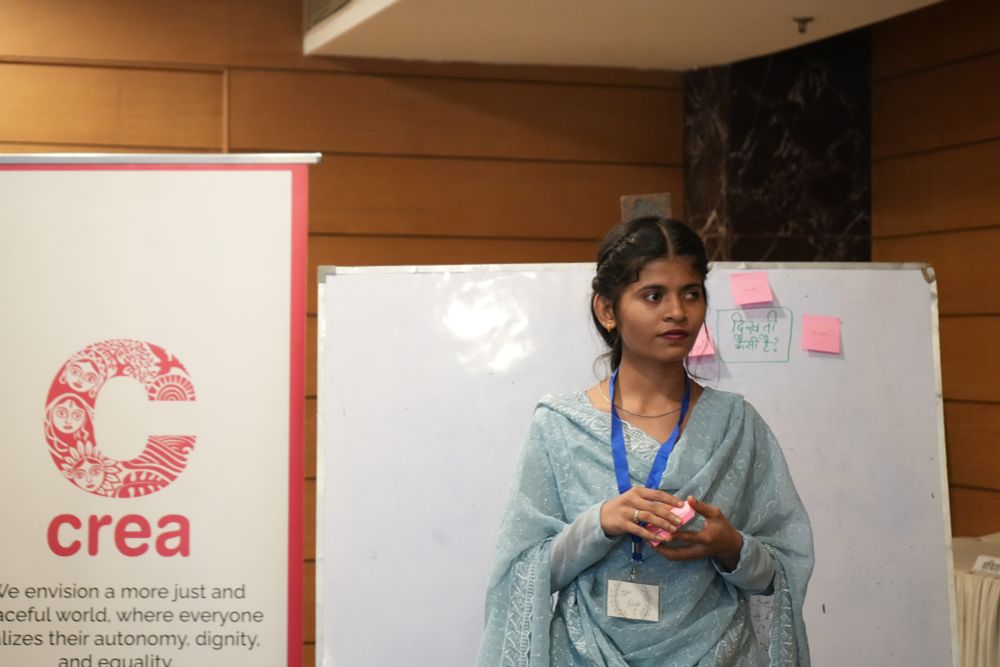 A participant in a blue salwar kurta at the Disability, Sexuality, and Rights (Hindi) Institute 2025. There's aboard with sticky notes behind her and on her left is the poster with the CREA logo