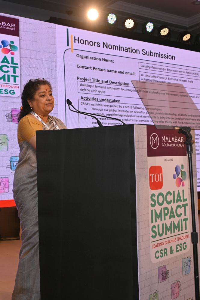 Anuradha Chatterjee on stage, accepting the Times of India’s Leadership in Advancing Gender Equality award for CREA. The podium features the Times of India and Malabar logos, with a projector screen in the background.