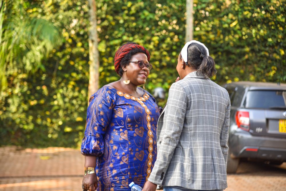  Two attendees engage in a thoughtful outdoor conversation during The Kimeeza 1st Edition, co-created by CREA and Femme Forte. One wears a deep blue patterned dress and the other wears a grey checked blazer. Trees and a car park form the background.
