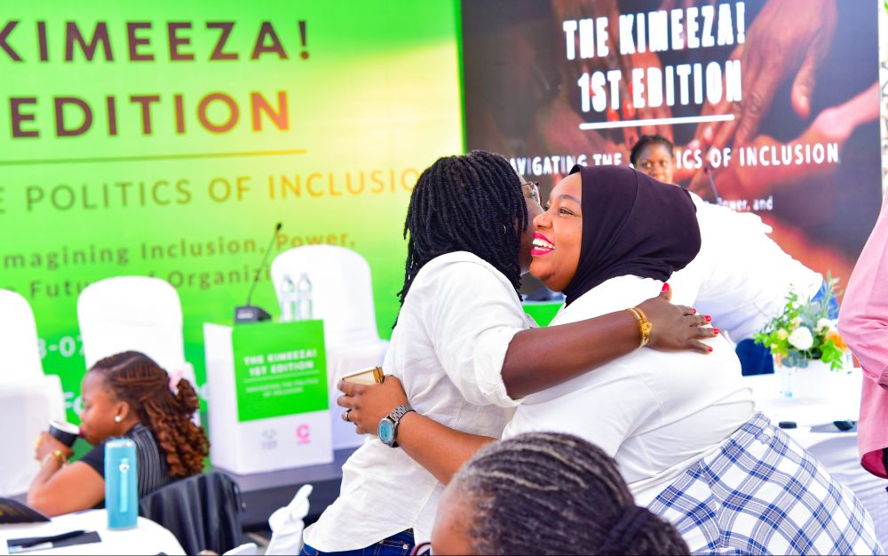 Two participants warmly embrace and smile at each other during The Kimeeza 1st Edition, co-created by CREA and Femme Forte. The background features event branding with the theme “Navigating the Politics of Inclusion.” Other attendees are visible, creating a vibrant and welcoming space.