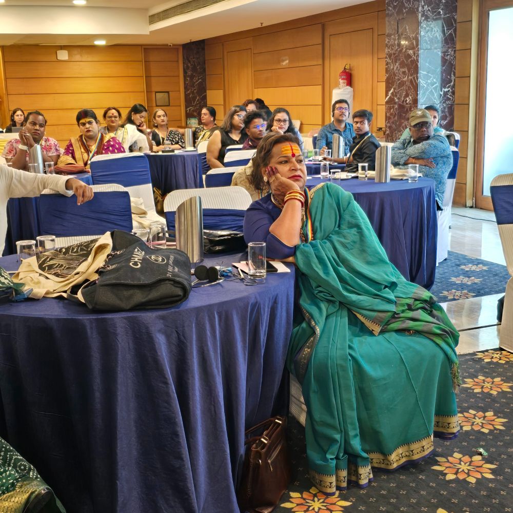 
Image of a participant in a green saree and a blue blouse sitting with their hand rested on a round blue table. Other participants are visible in the background
