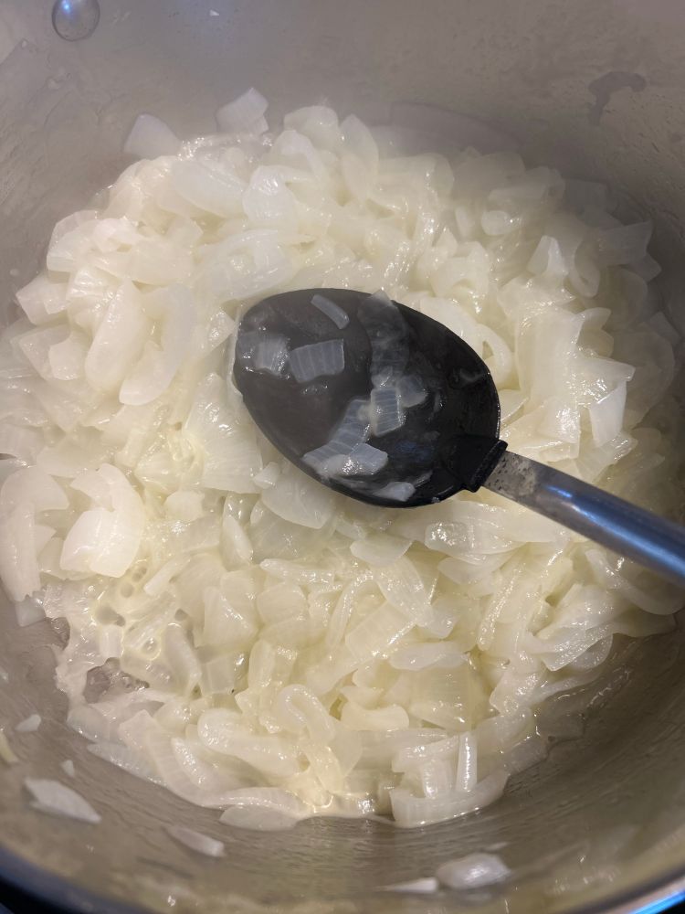 Onions cooking in a pot with a black spoon in the pot leaning against the side. 