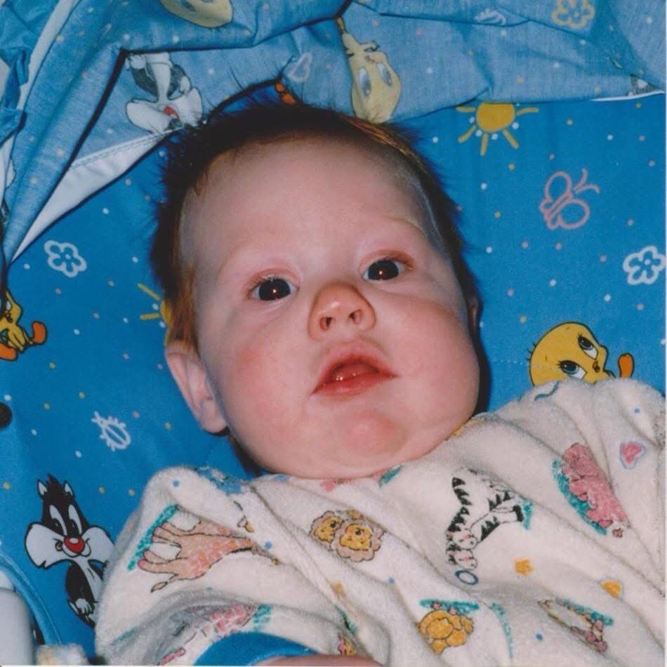 A baby with red hair sitting in a bouncy seat. 