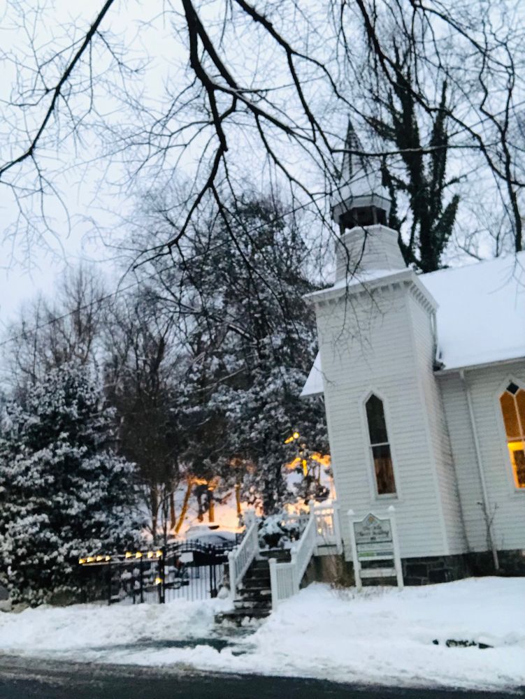 A white wooden church in snow with snow covered trees at sunset.