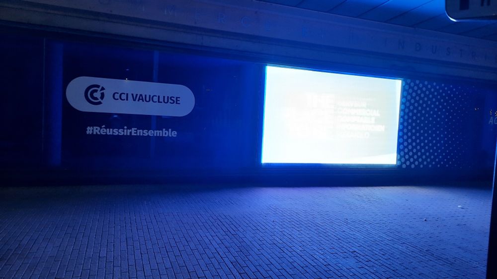 Un grand écran publicitaire allumé la nuit en vitrine de la CCI Vaucluse. Une lueur bleue inonde le trottoir à 5h00 du matin