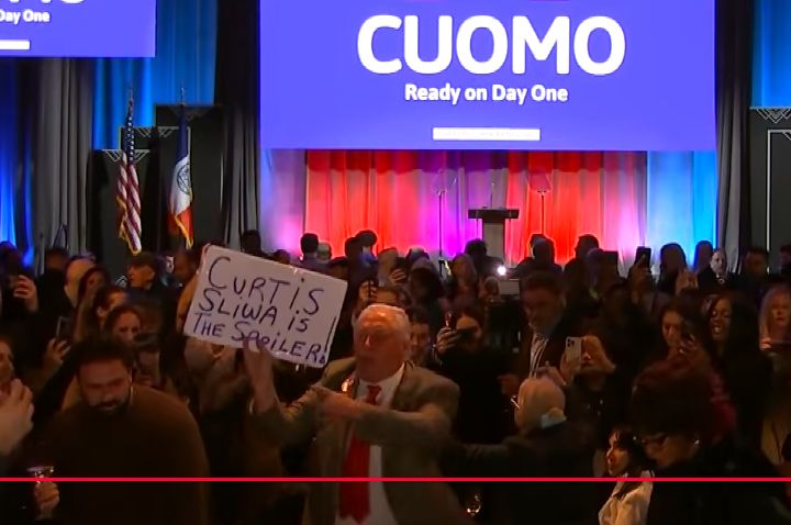 A rotund pink man (same approximate shade as hotel prime rib) waving a hastily handmade "CuRTiS SLiWA iS THE SPoiLER!" sign around at Cuomo's "Ready on Day One" failure gathering