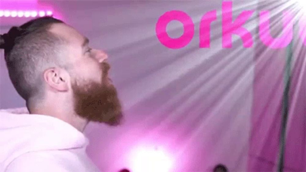 a man with a beard is standing in front of a pink background with the word orku .