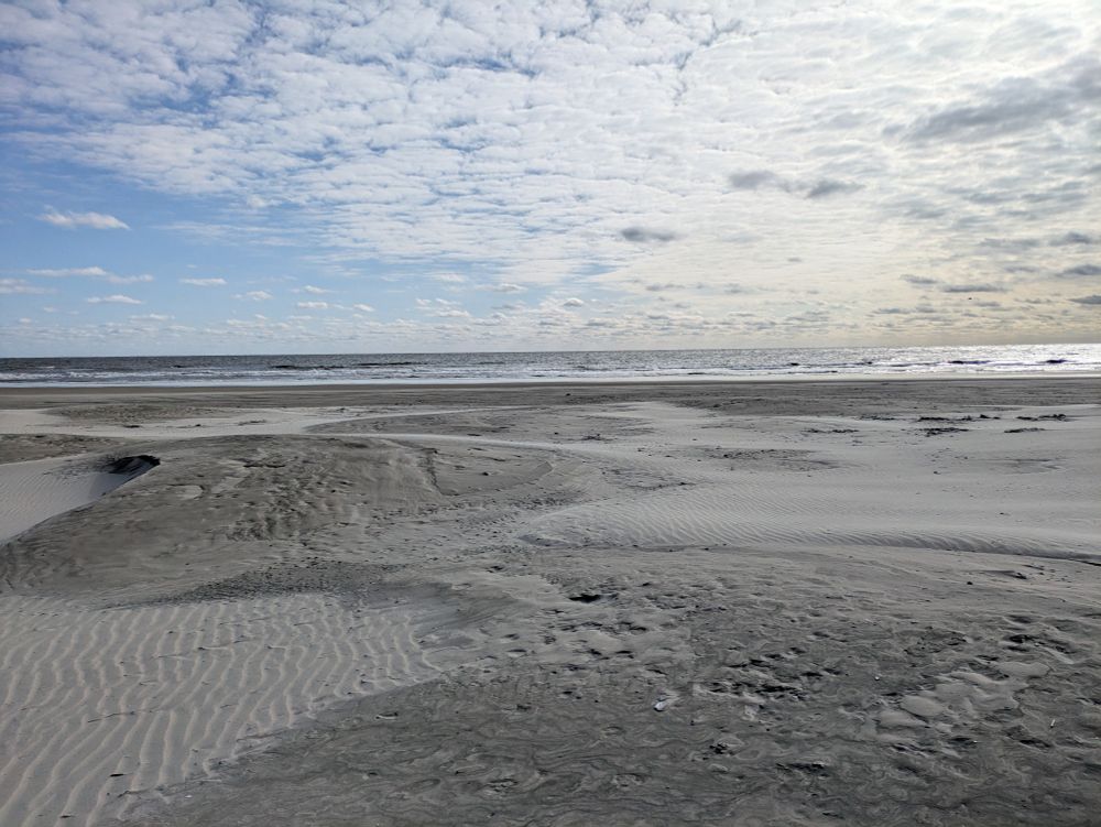 Picture of the sand and sea with clouded sky looking desolate.